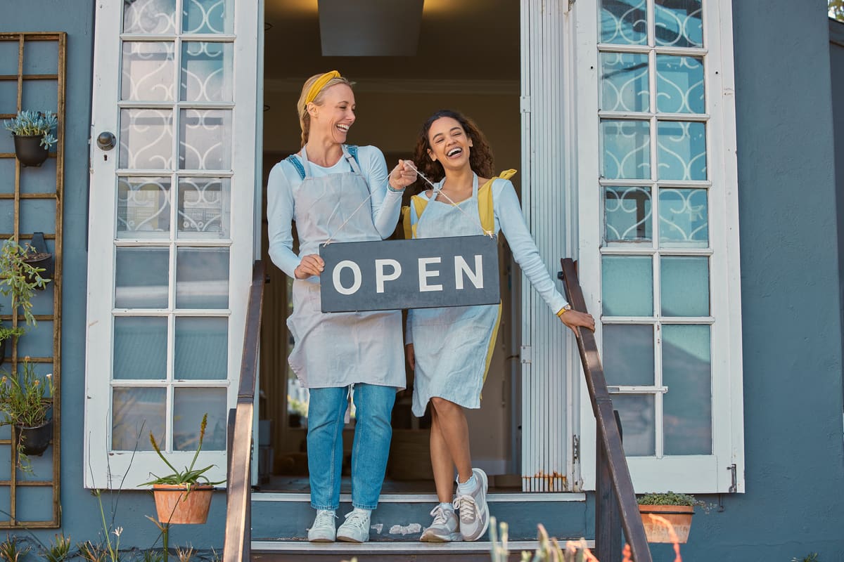 A picture of two women shop owners holding an open sign